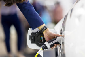 a female hand holding an electric car charger and connecting it to the charging point of an electric vehicle.