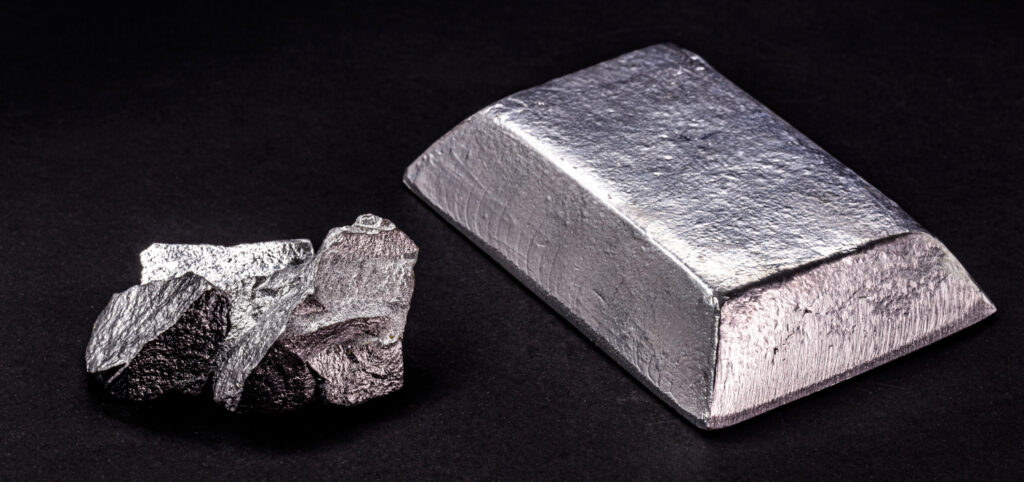 A raw zinc nugget next to a zinc ingot on a black background